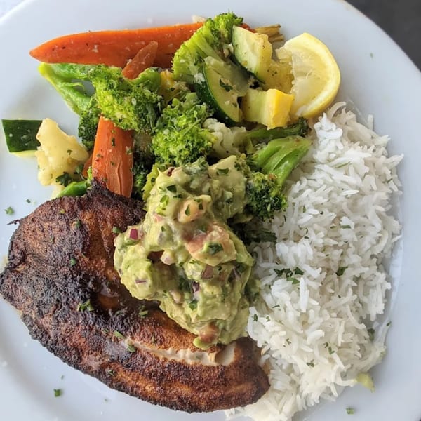 Blackened fish with guacamole, white rice, and steamed vegetables including broccoli, carrots, and zucchini.