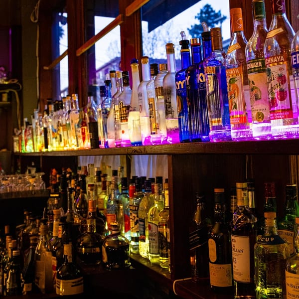 Liquor bottles on a bar shelf, illuminated by colorful LED lights, with a window in the background.