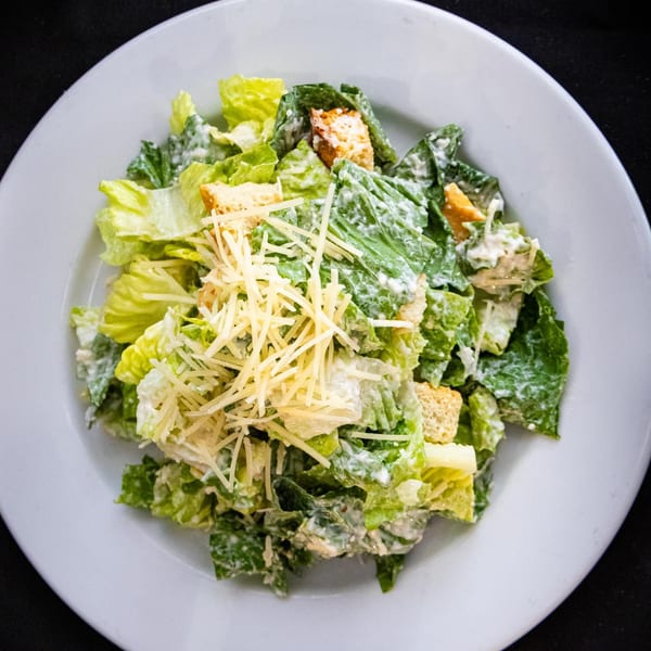 A Caesar salad with romaine lettuce, croutons, and shredded Parmesan cheese on a white plate.