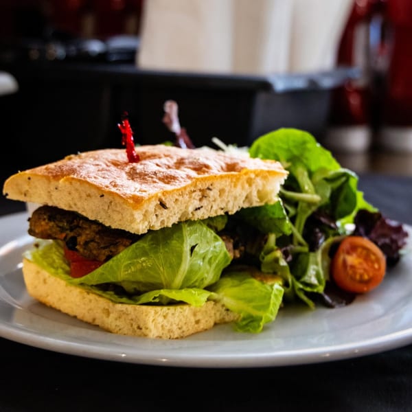 A focaccia sandwich with a patty, lettuce, and tomato, served with a side salad.