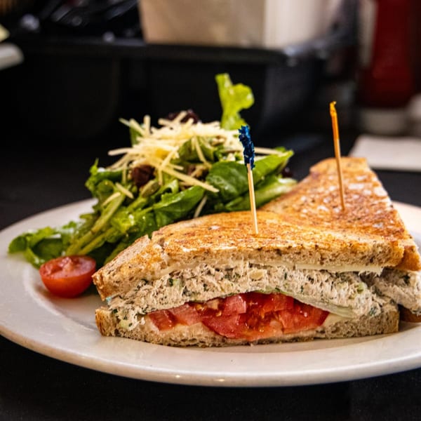 Grilled tuna melt sandwich with tomato and lettuce, served with a side salad.